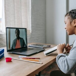 Side view of attentive ethnic girl listening to teacher explaining lesson online on laptop